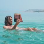 man floating on body of water while reading book