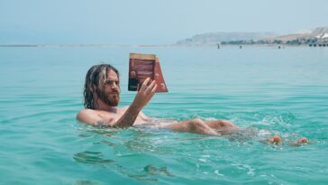 man floating on body of water while reading book