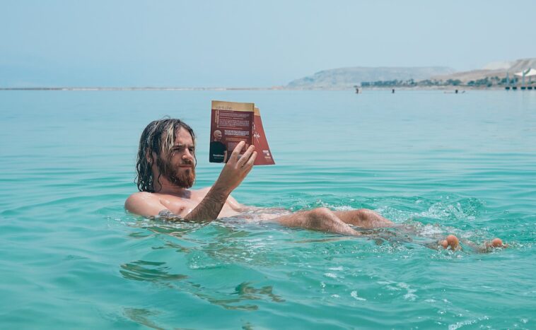 man floating on body of water while reading book