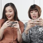 two women holding controllers sitting on sofa chair