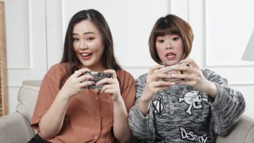 two women holding controllers sitting on sofa chair