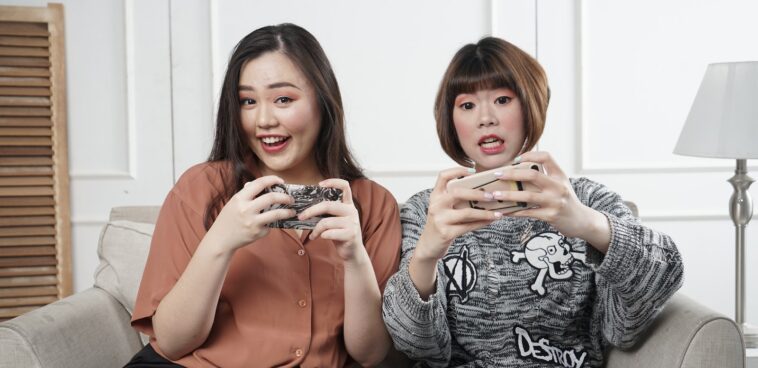 two women holding controllers sitting on sofa chair